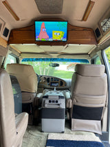 Experience cozy travel in this rv rental. Interior view shows overhead TV with cartoons, a portable cooler, and AC unit for comfort.