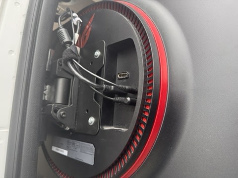 RV rental monitor connections: Rear view of a display, showing plugged-in cables (HDMI, audio, USB-C) and mounting bracket.