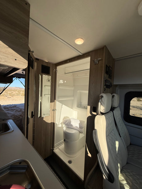 Bright RV rental interior: compact wet bath, kitchen sink, and bed area, with desert views.
