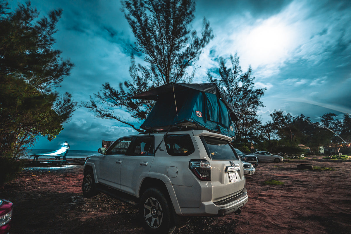 This white SUV with a deployed rooftop tent at a scenic ocean campsite, ready for an RV rental adventure. — photo 8