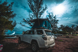 This white SUV with a deployed rooftop tent at a scenic ocean campsite, ready for an RV rental adventure.