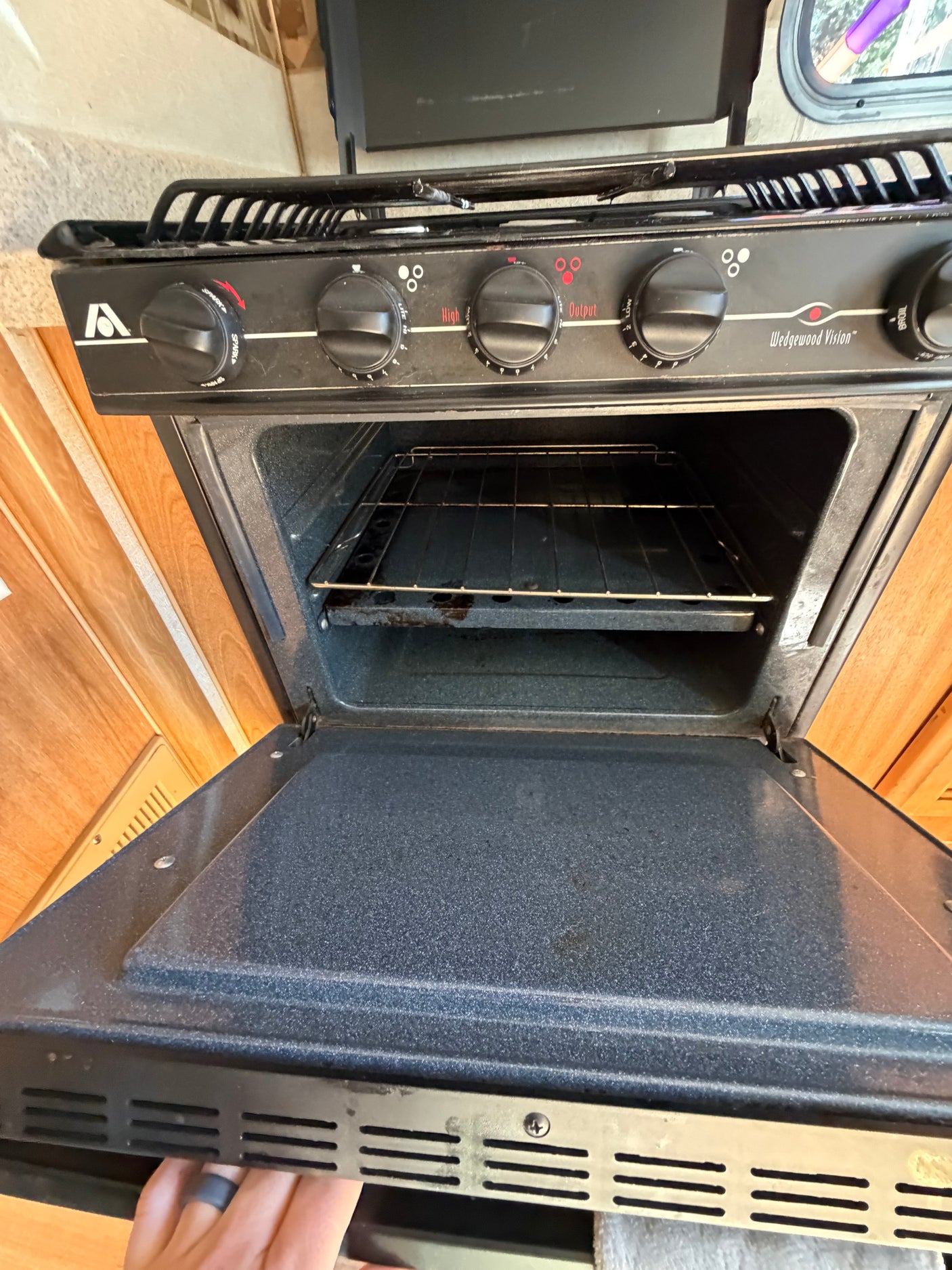 RV rental kitchen: Black gas stove and oven with open door, showing controls for burners and oven. Wedgewood Vision model.