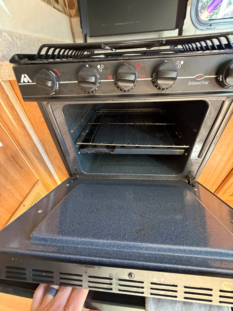 RV rental kitchen: Black gas stove and oven with open door, showing controls for burners and oven. Wedgewood Vision model.
