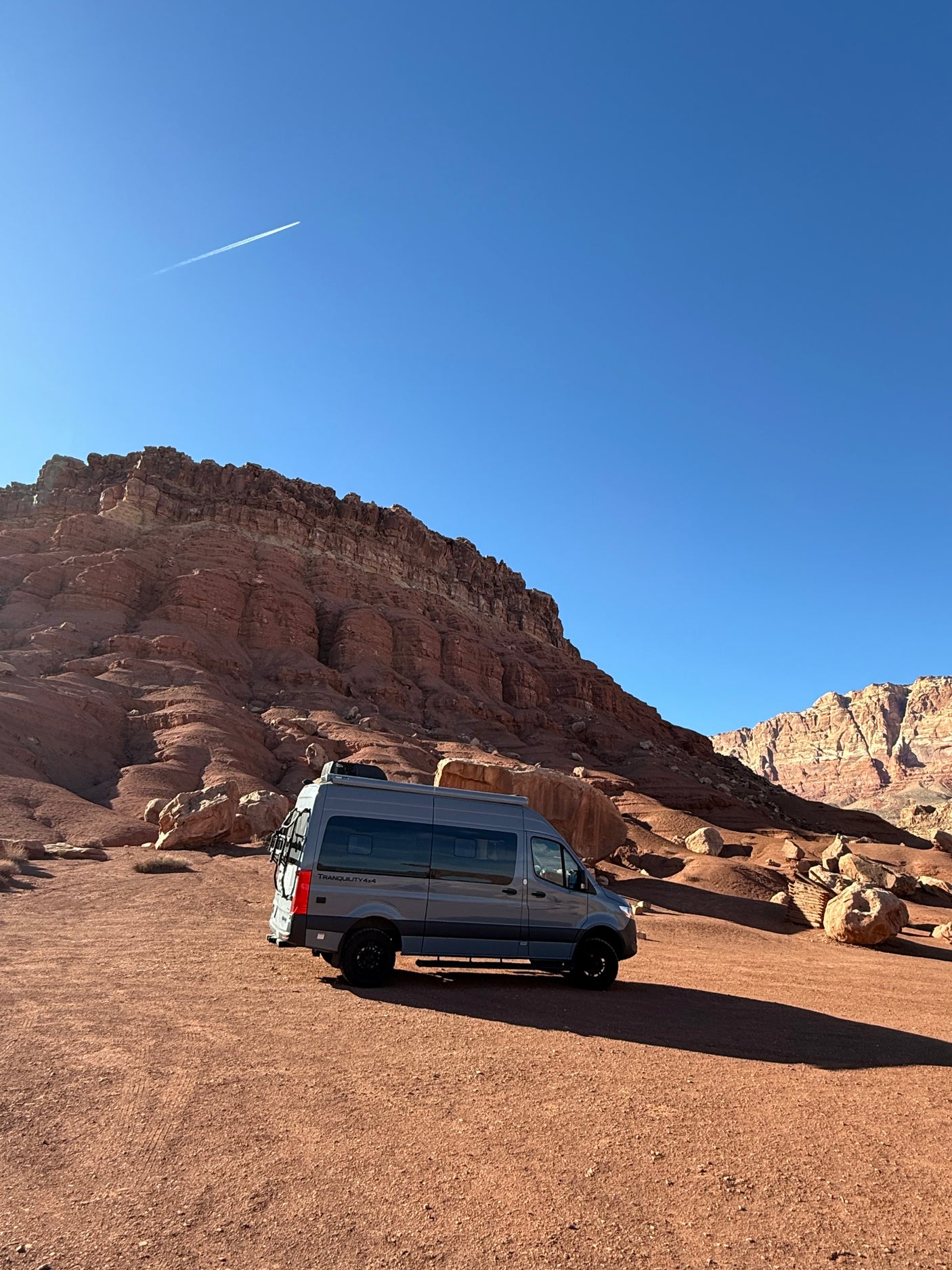 Grey RV rental parked in a desert landscape with towering red rock cliffs under a clear blue sky.
