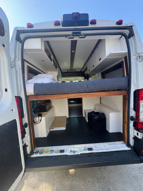 RV rental: Bright camper van interior seen from rear, featuring an elevated bed with storage below.