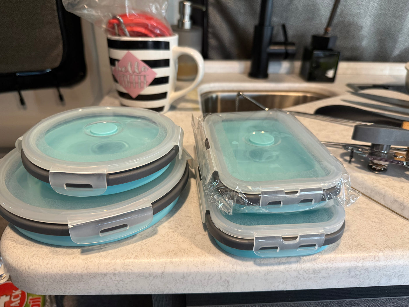 New collapsible food storage containers for an RV rental kitchen counter, with a striped coffee mug and sink.