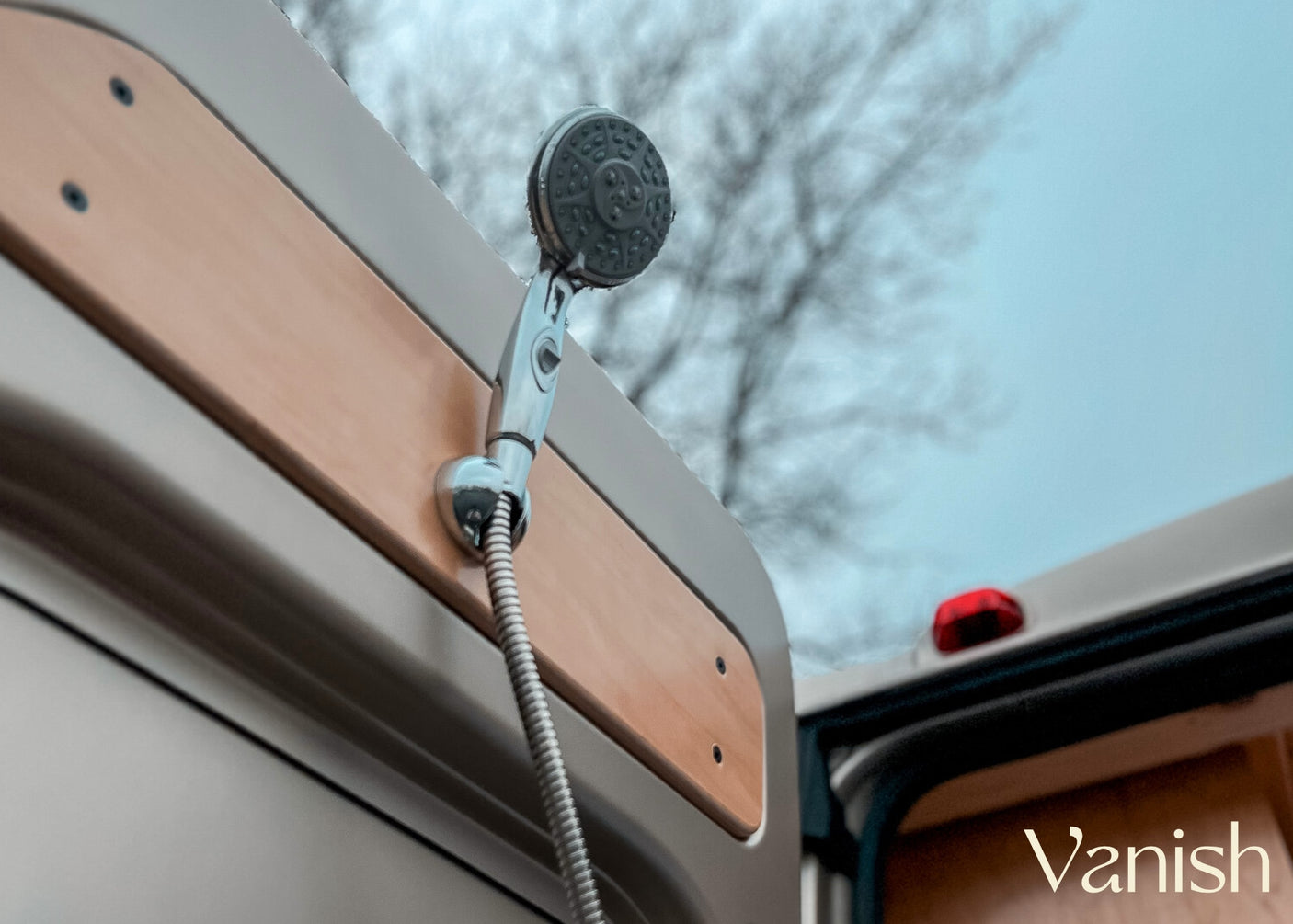 Close-up of an outdoor shower on an RV rental, mounted on a wooden panel, against a cloudy sky. Ideal for adventure travel.