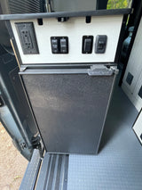 RV rental interior showing a Nova Kool fridge below a panel with GFCI outlet and awning switches.