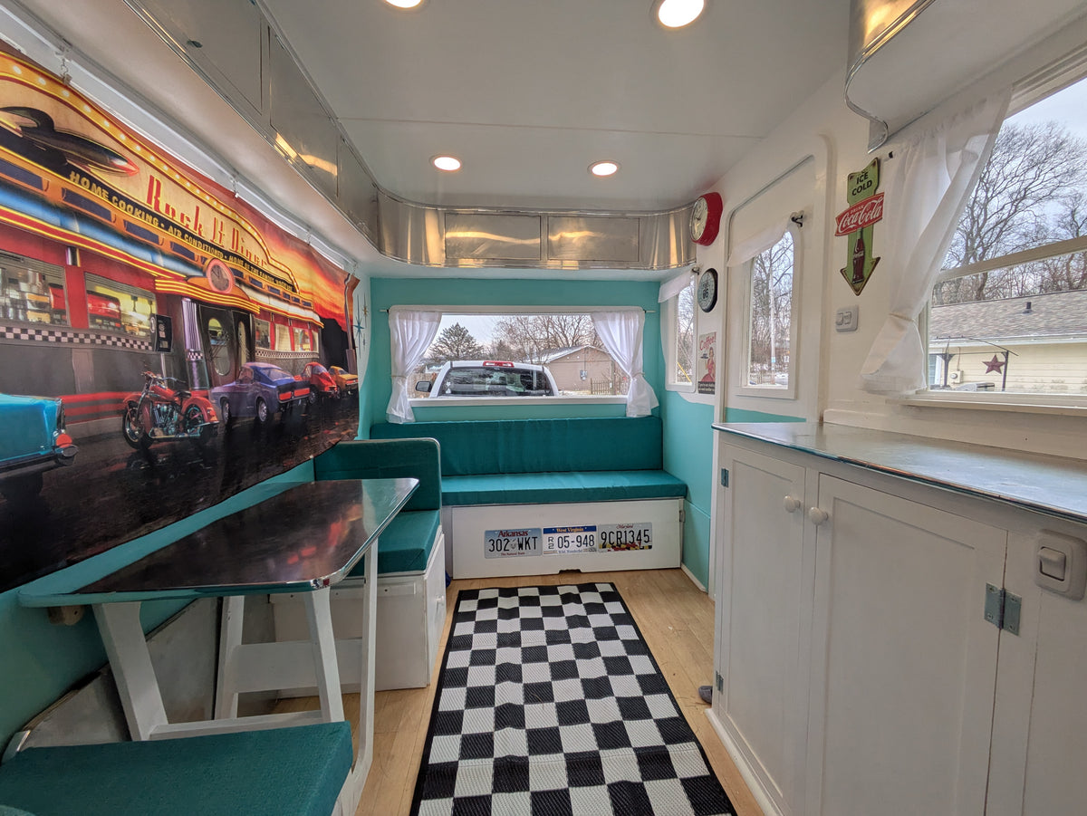 This retro diner-themed RV rental interior features teal booth seating, a checker rug, license plates, and a "Rock n Diner" mural. — photo 8