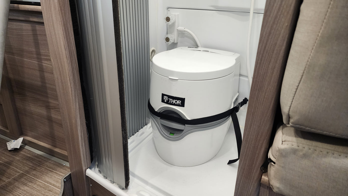 Inside an RV rental, a compact bathroom features a white portable toilet secured in a shower stall, ready for camper adventures.