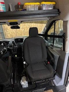 Inside an RV rental: Front cabin with driver's seat, dashboard, and overhead storage shelf clearly visible.