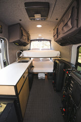 RV rental: Camper van interior with bunk beds, kitchen, storage, and folded seating. Carpeted floor, ceiling lights.