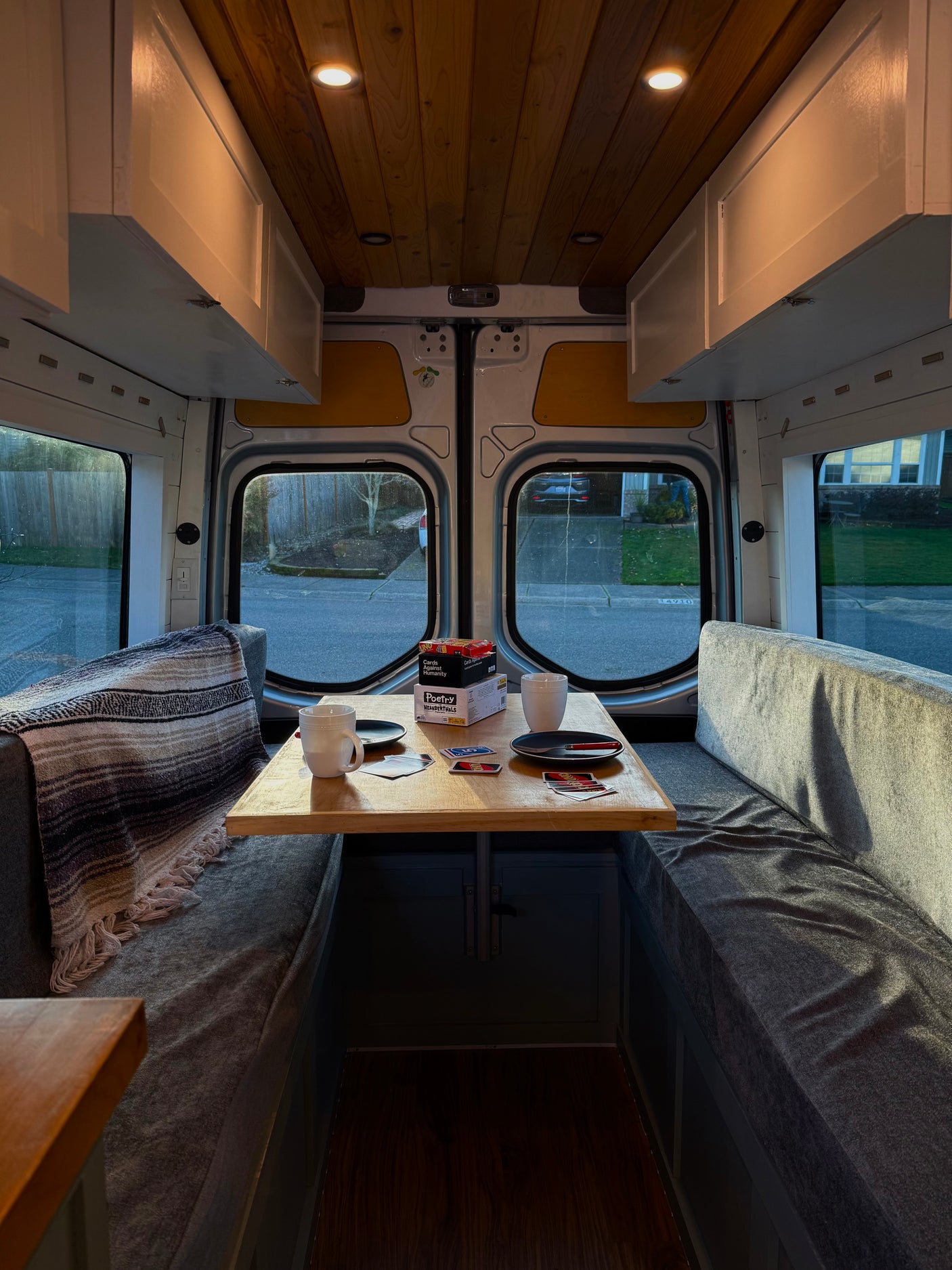 This RV rental interior offers a cozy dining space with games, comfy seating, wood ceiling, and warm lights. Great for travelers.
