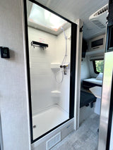 RV rental: Bright shower with digital thermostat, clear door, and a cozy sleeping area visible beyond.
