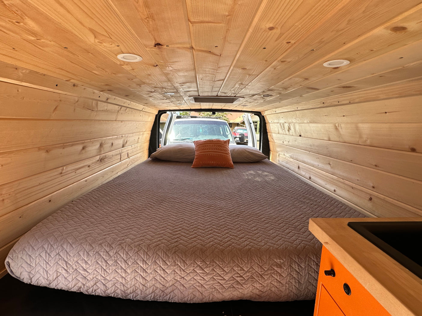 Inside this camper van RV rental, enjoy a comfortable bed, warm wood paneling, and a compact kitchen.
