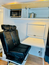 RV rental interior: space-saving design with microwave, comfortable seating, and a wall-mounted table for compact living.