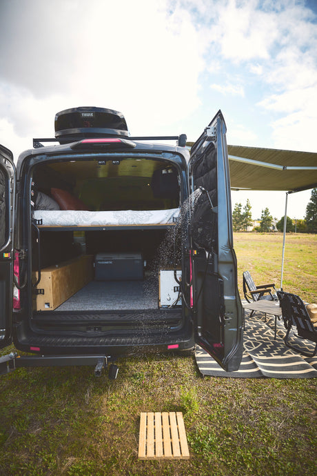 Experience comfort with this rv rental! A camper van with an outdoor shower, cozy bed, and shaded outdoor seating area for camping.