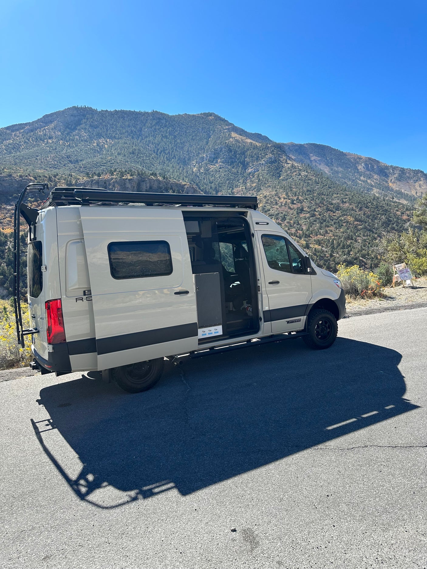 White camper van RV rental parked on a scenic mountain road with doors open. Perfect for an outdoor adventure trip.