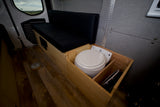 Explore this RV rental's clever design: a comfortable black bench, wood storage, and a neatly recessed portable toilet.