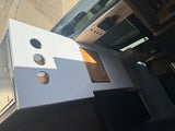 RV rental: Custom camper van interior with a white countertop, round cutouts, wood insert, & overhead controls.