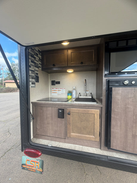 This RV rental features a convenient outdoor kitchen with a sink, stovetop, microwave, and small fridge.