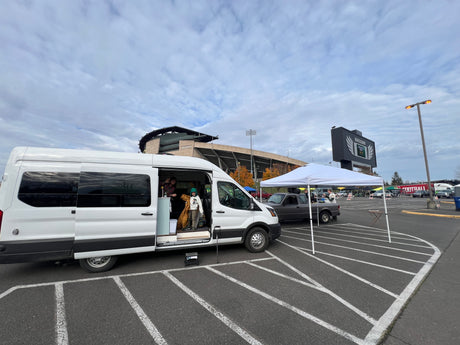 White RV rental camper van parked at a stadium, with people inside for a tailgate event. Ideal for game day experiences.