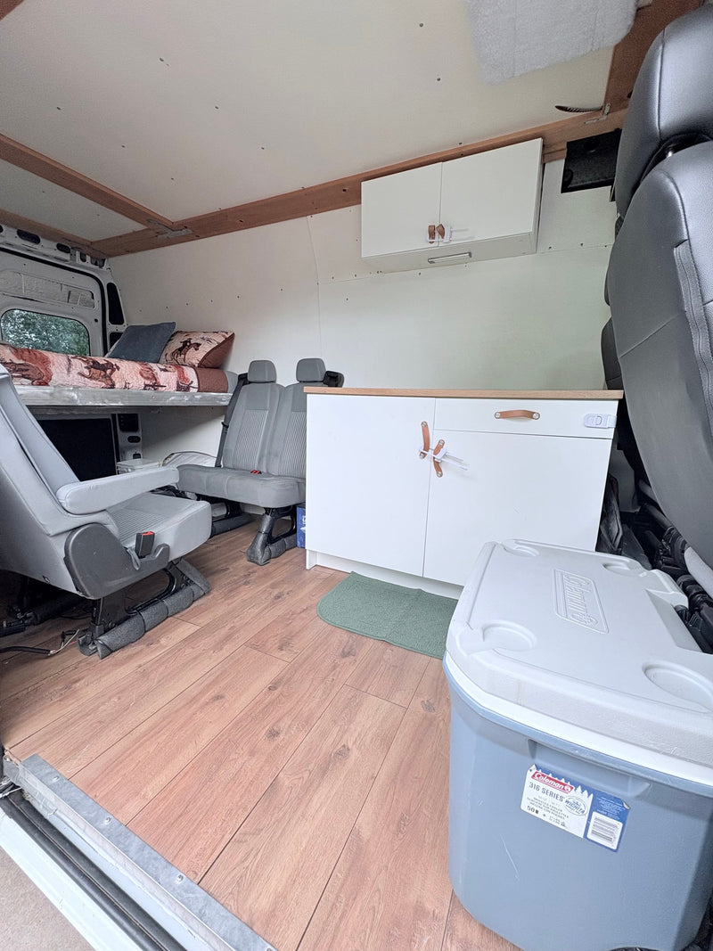 Inside an rv rental: custom van interior with an elevated bed, gray seating, and storage, including a Coleman cooler. — photo 3
