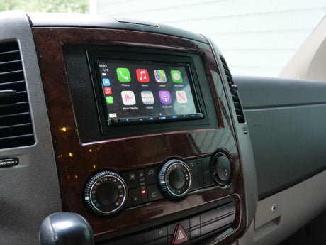 RV rental dashboard: Kenwood Apple CarPlay stereo displaying apps, flanked by air vents, with climate controls below.