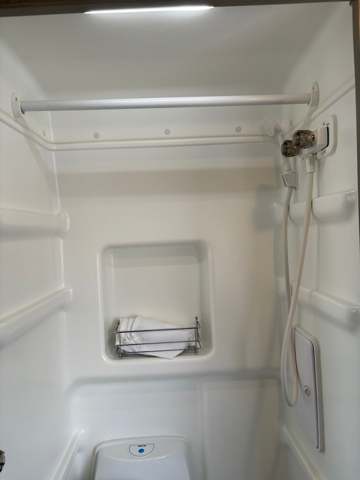 This RV rental bathroom features a compact shower, toilet, and mounted basket, designed for efficient travel comfort.