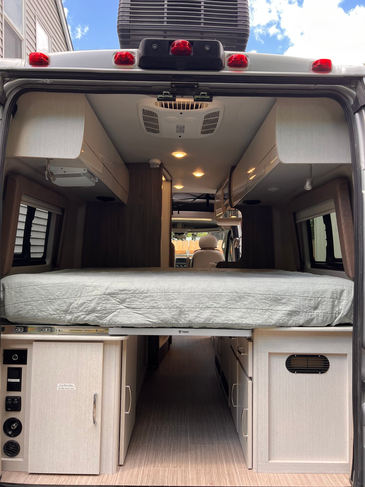 RV rental: View of the camper's spacious interior looking forward, featuring a raised bed, central aisle, and controls. — photo 3