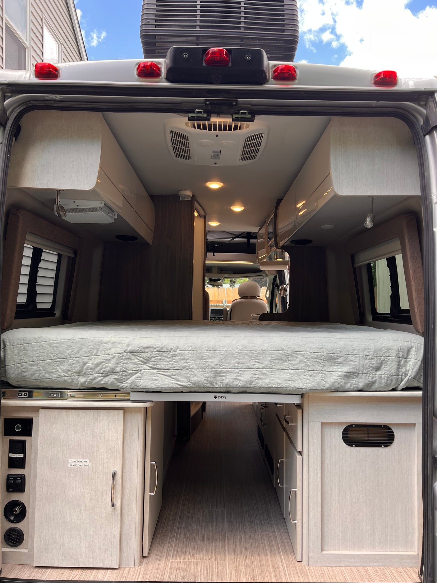 RV rental: View of the camper's spacious interior looking forward, featuring a raised bed, central aisle, and controls.