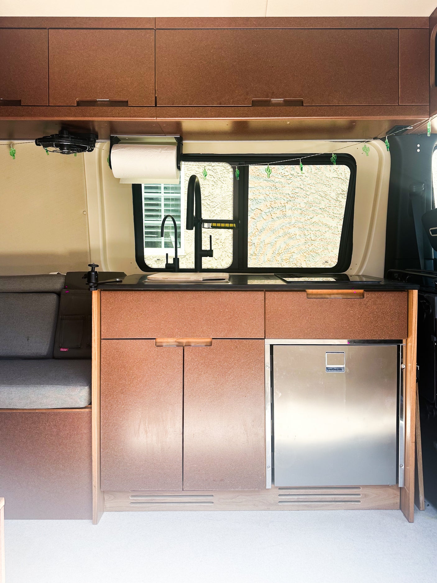 Modern rv rental interior: compact kitchen with sink, fridge, overhead cabinets, and comfy bench seating.