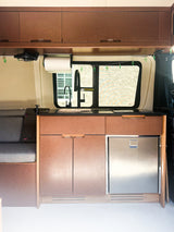 Modern rv rental interior: compact kitchen with sink, fridge, overhead cabinets, and comfy bench seating.