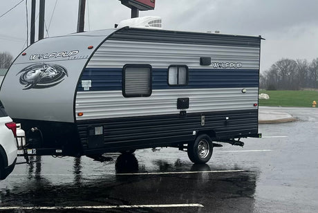 A sleek grey and blue Wolf Pup travel trailer, great rv rental for outdoor adventures, parked on a rainy day.