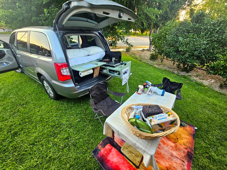 This RV rental shows a minivan converted for camping with a bed, pull-out kitchen, and an outdoor dining setup.