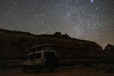 RV rental camper van parked under a dazzling, star-filled night sky in a vast desert landscape.