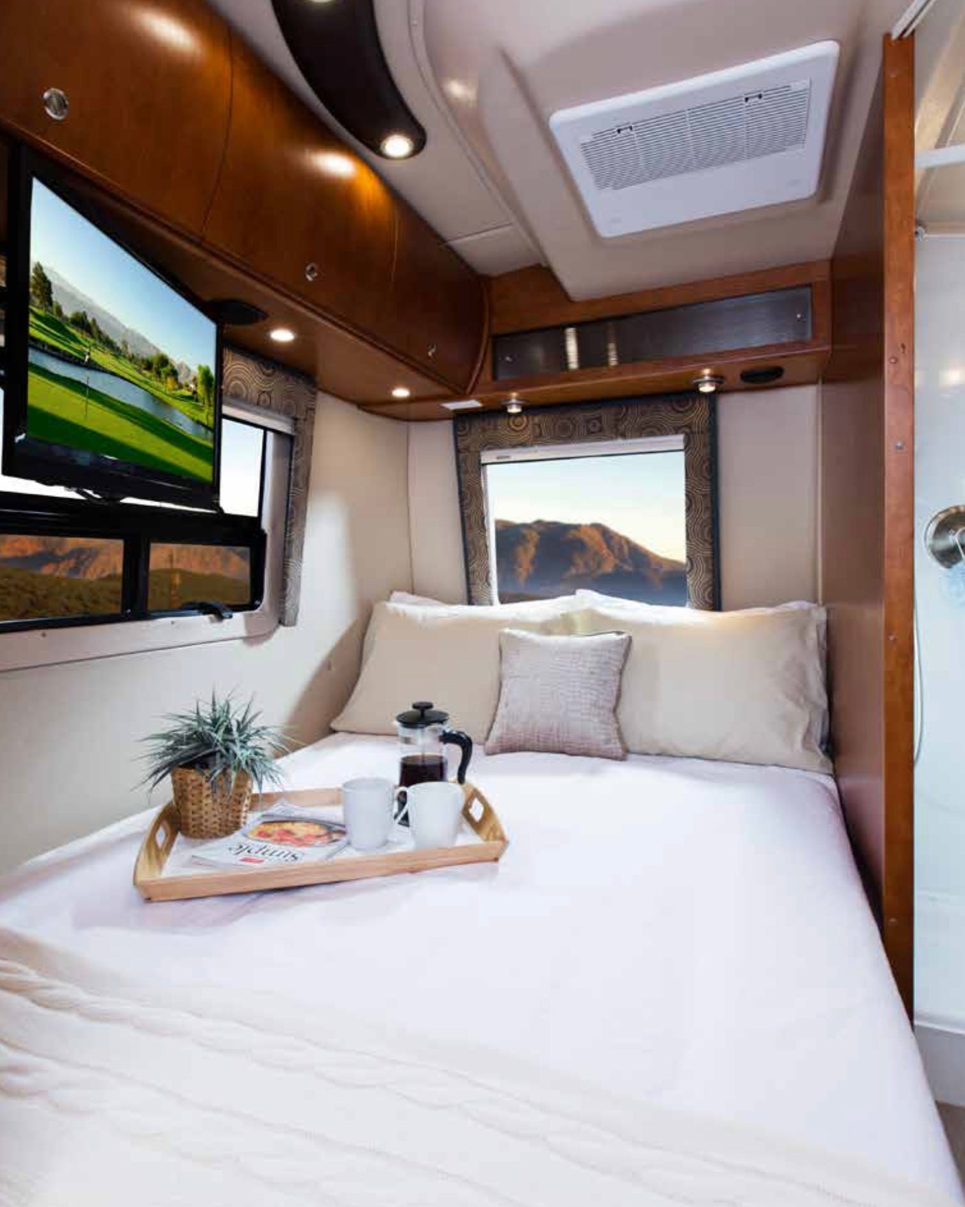 Cozy RV rental bedroom interior features a comfortable bed, breakfast tray, and mountain views, ideal for travel.