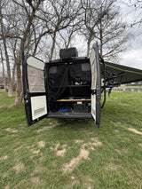 RV rental camper van, rear doors open, showing storage, bug screen. Parked lakeside with awning & bike rack ready for outdoor adventure.