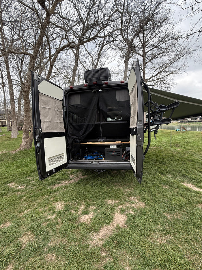 RV rental camper van, rear doors open, showing storage, bug screen. Parked lakeside with awning & bike rack ready for outdoor adventure.