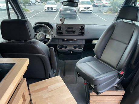 RV rental: Inside a Mercedes Sprinter camper van, showing the cockpit, dashboard, swivel passenger seat, and wood counter.