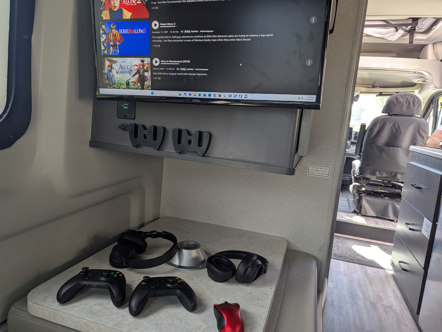 An RV rental's entertainment hub, featuring game controllers, headphones, and a TV displaying movie selections like Home Alone 3.