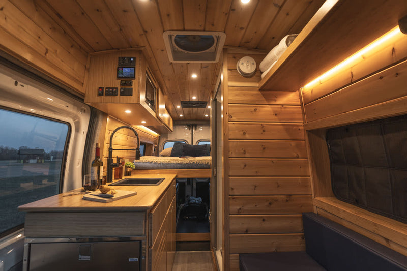  and ample storage for your road trip.|White Ford Transit camper van RV rental in a golden field. Side door open shows custom wood interior — photo 16
