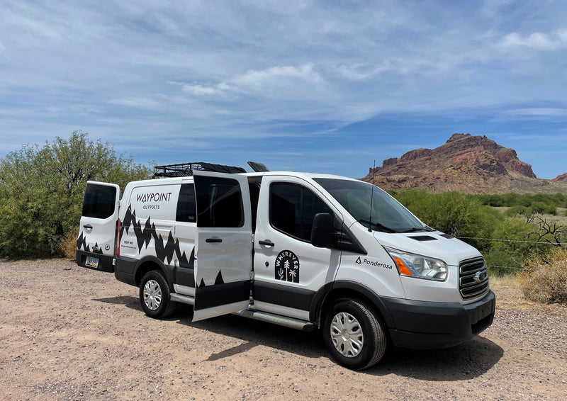 White Waypoint Outposts RV rental van with mountain graphics, doors open, parked in a desert with mountains. — photo 6