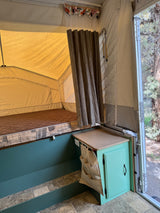 Experience a comfortable RV rental interior with a bed, mint green cabinet, and outdoor view in this pop-up camper.