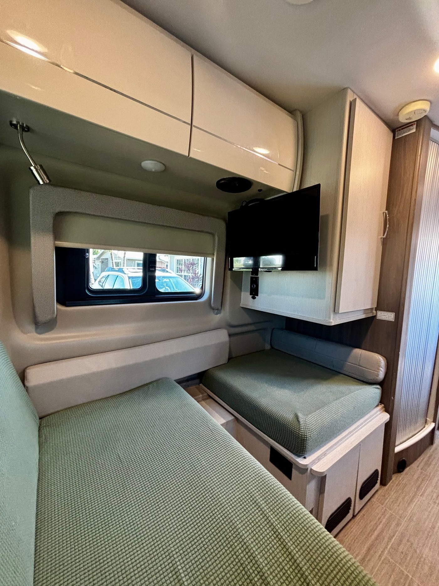 Inside an RV rental: a modern dinette area with sage green cushions, overhead storage, and a mounted TV. — photo 16