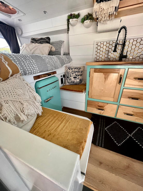 This cozy rv rental camper van interior features a compact kitchen, comfortable bed, and a stylish retro fridge.