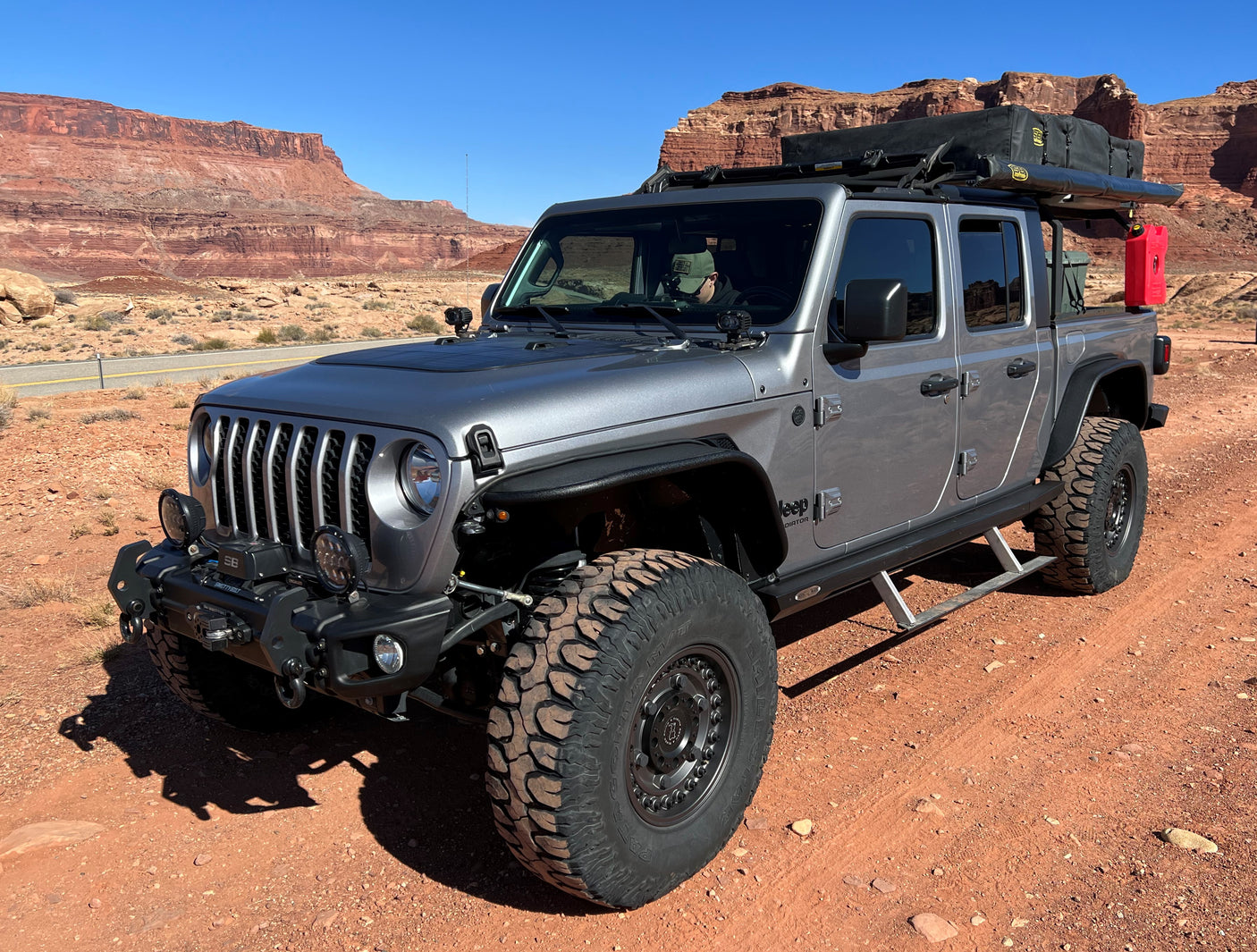 Rugged gray Jeep Gladiator, equipped for overlanding, parked in a red rock desert landscape. Consider this for an RV rental adventure.