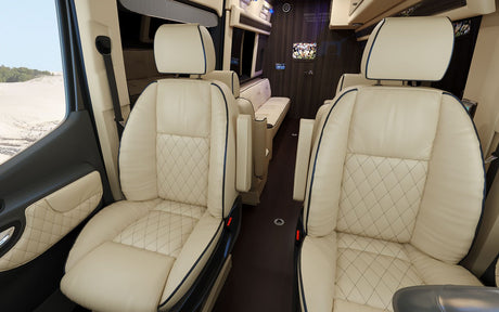 Inside a luxurious rv rental: cream quilted leather captain's chairs, armrests, TV showing sports, and a sandy dune landscape view.
