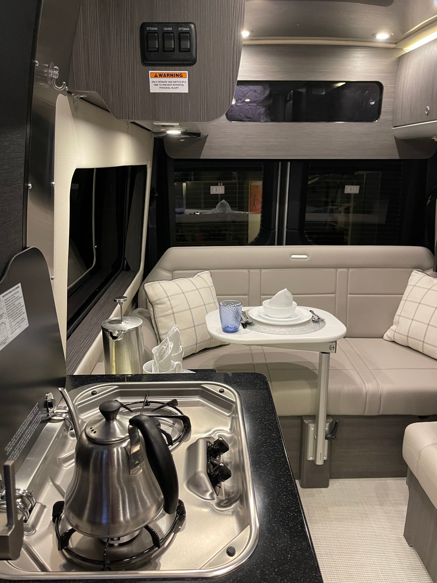 Inside an RV rental: a modern kitchen with stovetop, kettle, and an inviting lounge area with a small dining table.