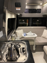 Inside an RV rental: a modern kitchen with stovetop, kettle, and an inviting lounge area with a small dining table.